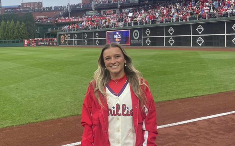 Cayla Kalani smiling, dressed in her Phillies gear on the first base line during a game