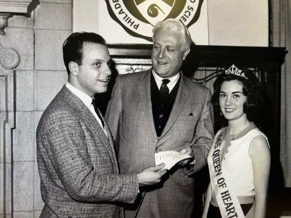 Sigma Phi Epsilon brother at a fundraiser with a female student wearing a crown and a sash that reads “1965 Queen of Hearts”